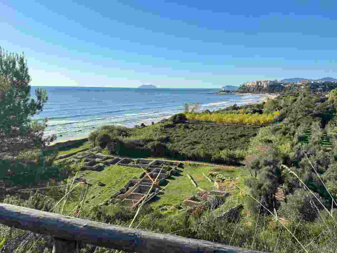 Vista panoramica sulla costa di Sperlonga con il mare azzurro, spiaggia sabbiosa, vegetazione rigogliosa e i resti archeologici della Villa di Tiberio in primo piano.